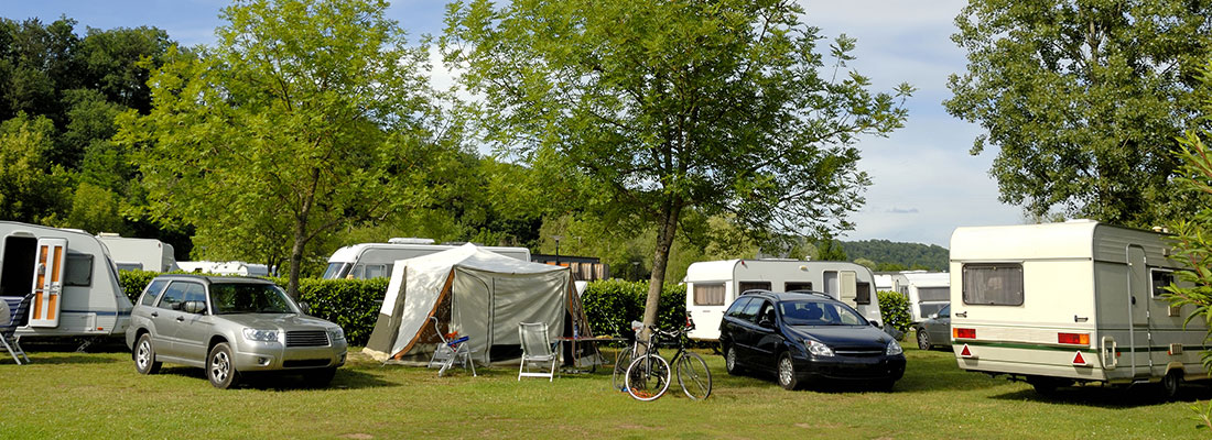 Mehrere Wohnwagen und Autos auf einem begrünten Campingplatz im Sommer