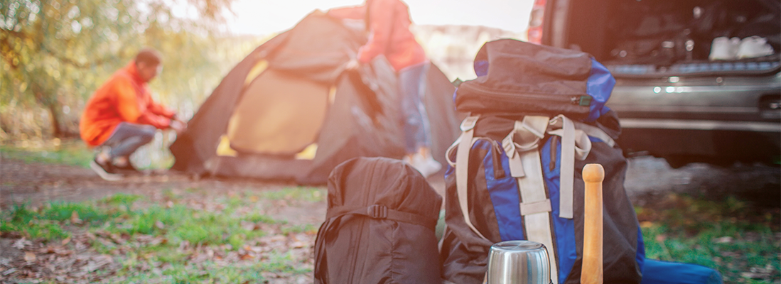 gepackte Campingsachen und Zeltaufbau im Hintergrund