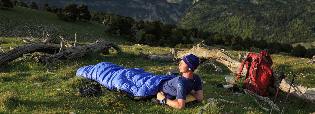 EIn Mann liegt mit einem Schlafsack in der Natur