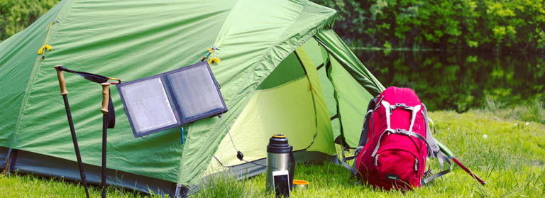 Grünes Zelt steht auf einer Wiese mit einem roten Rucksack und einer mobilen Solarzelle