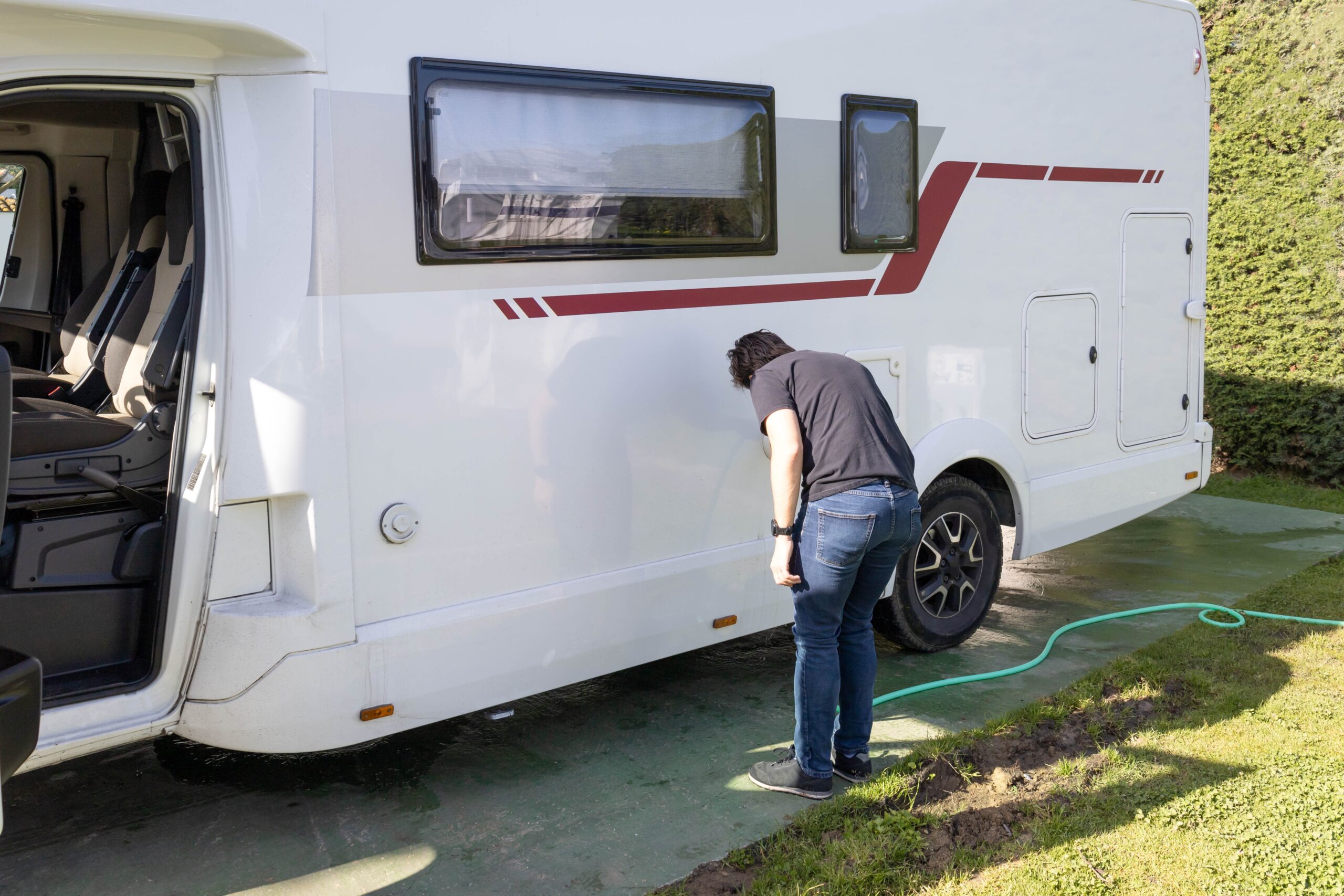 Unerkennbarer Mann, der die Instandhaltung des mobilen Hauses mit einem Schlauch, der das Wasser füllt