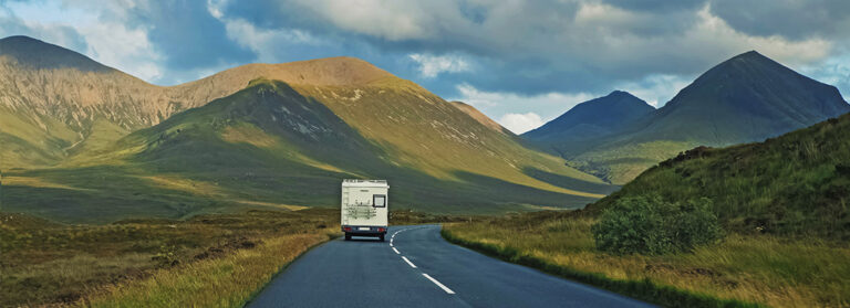 Weißer Campevan, der auf der linken Seite der Straße fährt, vorbei an den malerischen Hügeln in Schottland