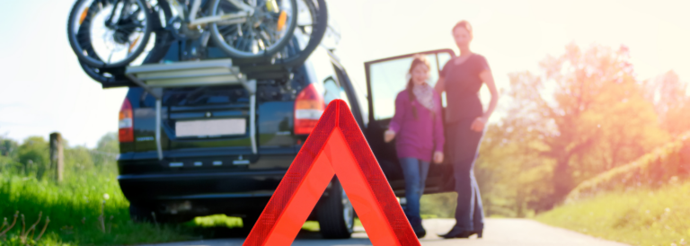 Warndreieck und Auto mit Fahrradträger am Straßenrand neben einer Wiese und Menschen-