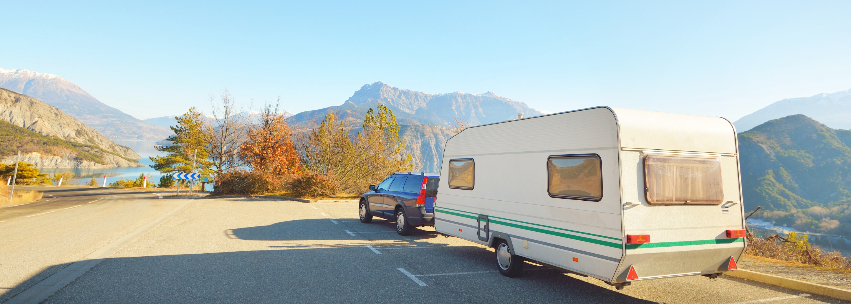 Auto und Wohnwagen fahren über Straße. Berge im Hintergrund.